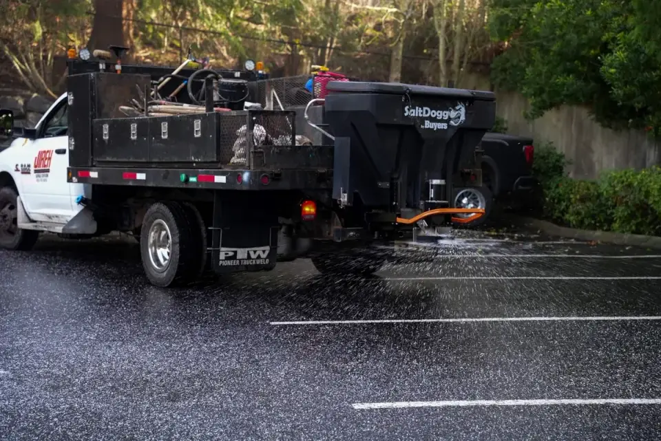 Spreader truck applying granular material across a striped parking lot in Western Washington