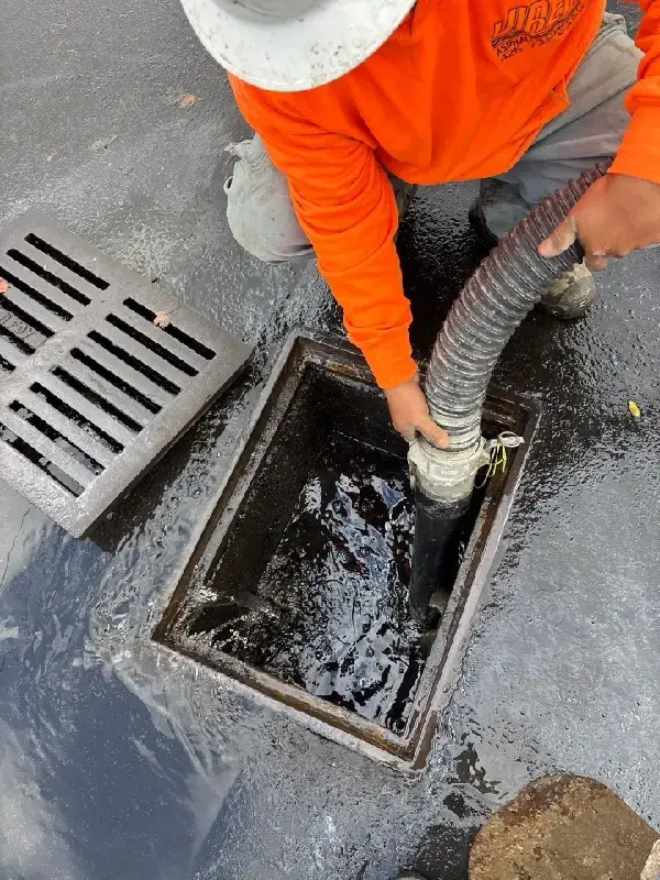Jireh crew member using a jet-vac hose to vacuum sediment and water from a parking lot catch basin