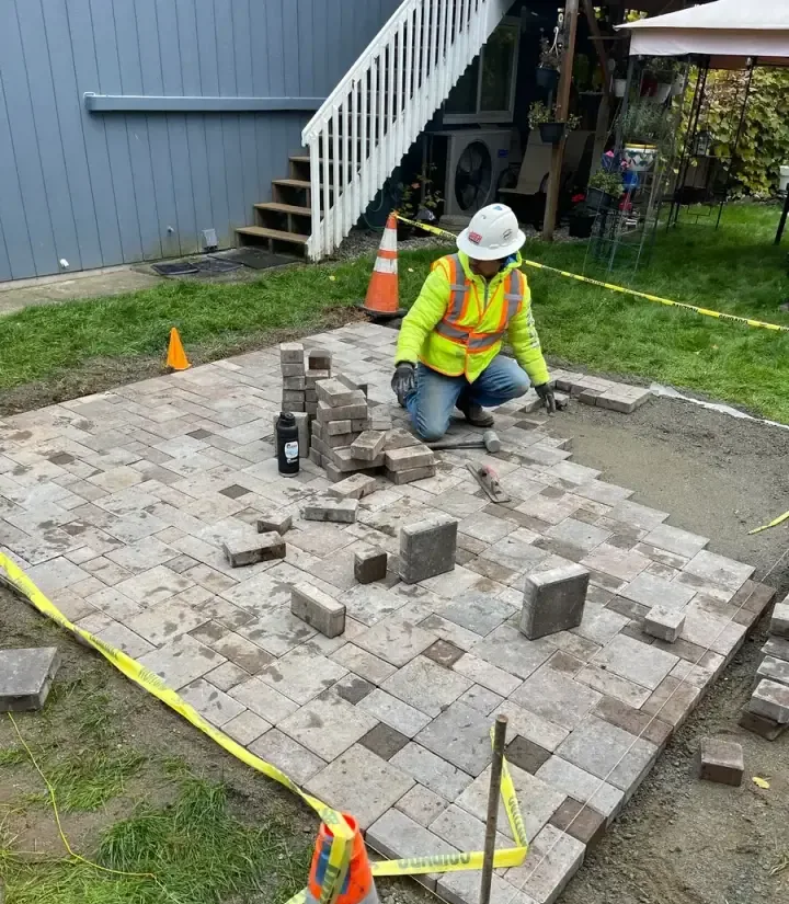 Jireh crew member laying concrete pavers in a patio pattern during a late-October installation in Western Washington