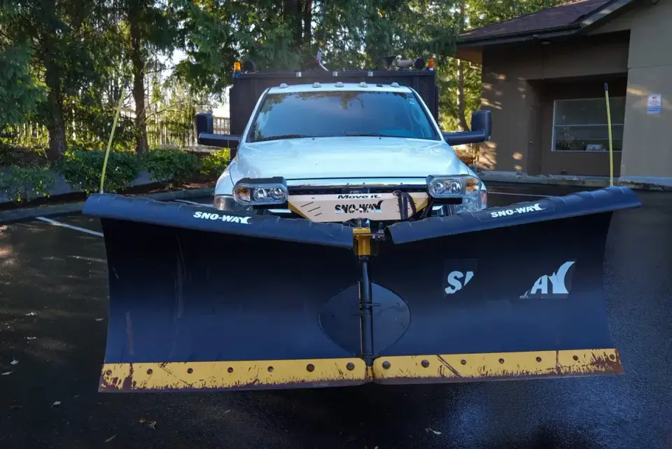 Snowplow truck with a V-plow staged in a wet commercial parking lot in Western Washington